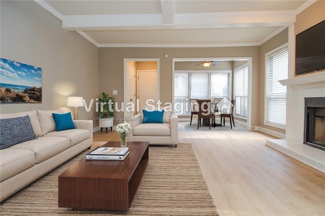 living area with beam ceiling, a fireplace with raised hearth, crown molding, and wood finished floors