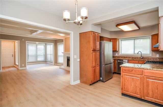 kitchen with a fireplace with raised hearth, a sink, light wood-style floors, appliances with stainless steel finishes, and brown cabinets