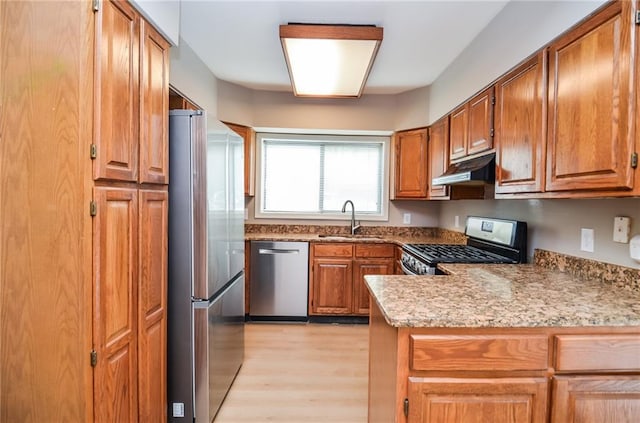 kitchen featuring light wood-style flooring, appliances with stainless steel finishes, brown cabinets, under cabinet range hood, and a sink