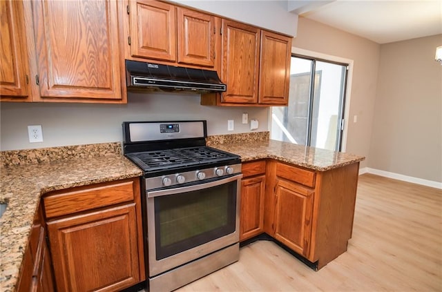 kitchen featuring stainless steel range with gas cooktop, light wood-style flooring, a peninsula, under cabinet range hood, and baseboards