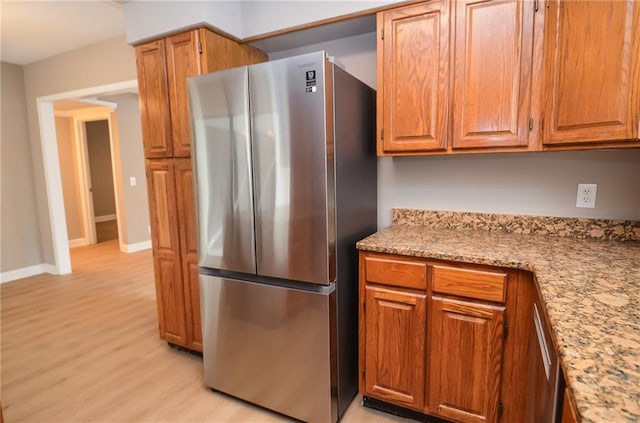 kitchen with light wood finished floors, brown cabinetry, freestanding refrigerator, light stone countertops, and baseboards