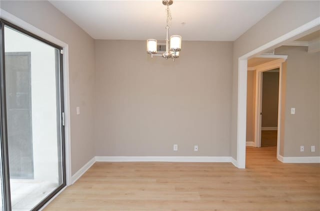 spare room with light wood-type flooring, baseboards, and a notable chandelier