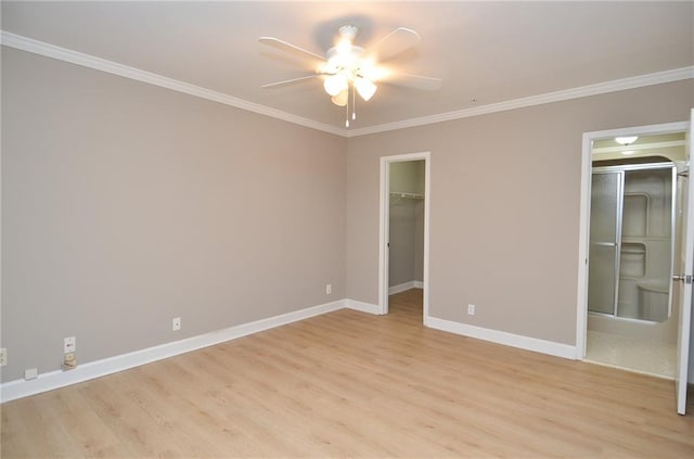 unfurnished bedroom with crown molding, a spacious closet, a ceiling fan, light wood-type flooring, and baseboards