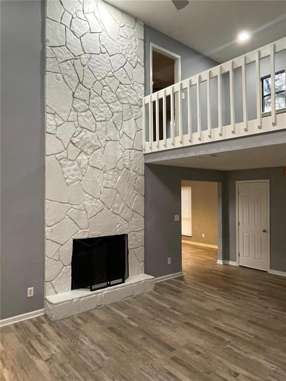 unfurnished living room featuring hardwood / wood-style floors, a towering ceiling, and a stone fireplace