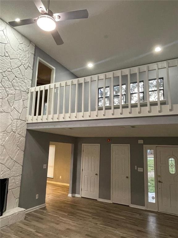 interior space featuring ceiling fan, a stone fireplace, wood-type flooring, and a high ceiling