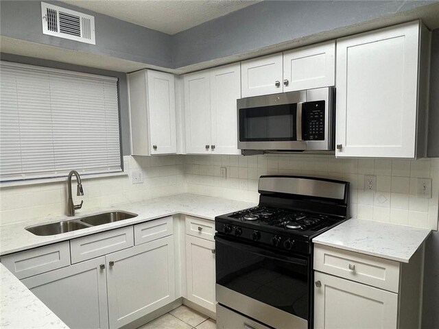 kitchen with tasteful backsplash, sink, white cabinets, and appliances with stainless steel finishes