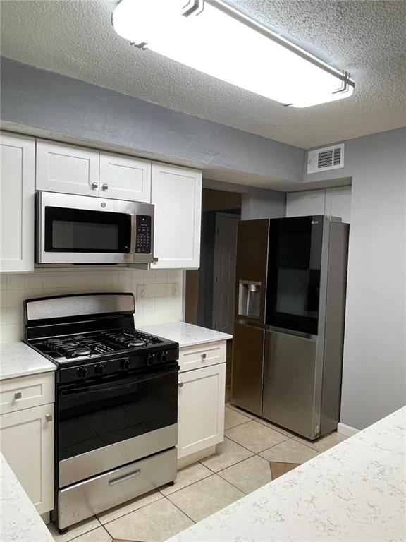 kitchen with decorative backsplash, white cabinetry, a textured ceiling, and appliances with stainless steel finishes