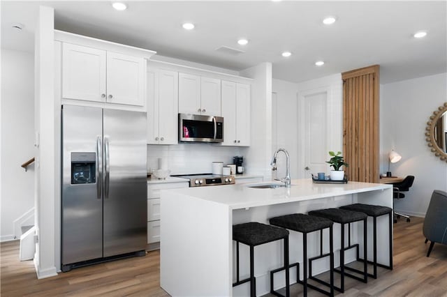 kitchen with hardwood / wood-style floors, a center island with sink, sink, white cabinetry, and stainless steel appliances