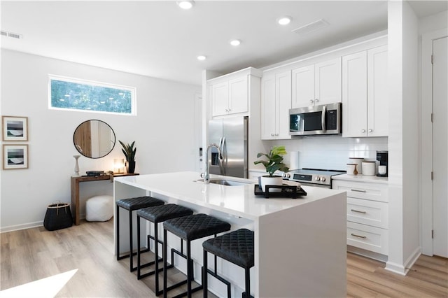 kitchen with white cabinets, stainless steel appliances, a kitchen island with sink, and a breakfast bar area