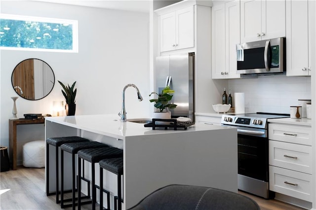 kitchen featuring white cabinetry, a center island with sink, stainless steel appliances, and light wood-type flooring