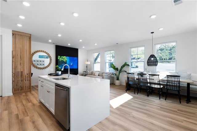 kitchen with stainless steel dishwasher, decorative light fixtures, light hardwood / wood-style flooring, white cabinets, and an island with sink