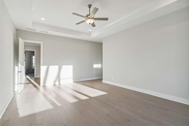empty room featuring a tray ceiling, baseboards, recessed lighting, wood finished floors, and ceiling fan