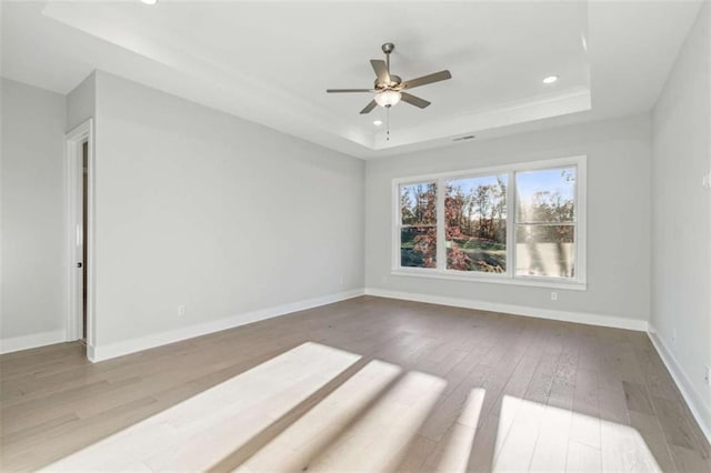 empty room with recessed lighting, a tray ceiling, wood finished floors, a ceiling fan, and baseboards