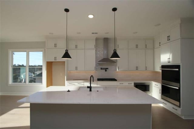 kitchen featuring built in microwave, a sink, tasteful backsplash, wall chimney range hood, and double oven