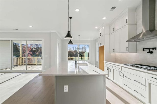kitchen featuring a sink, light wood-style floors, wall chimney exhaust hood, decorative backsplash, and stainless steel gas cooktop