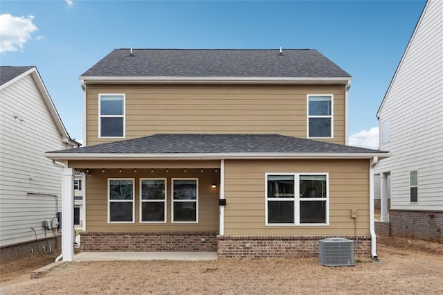 back of house featuring a shingled roof, central AC, and brick siding