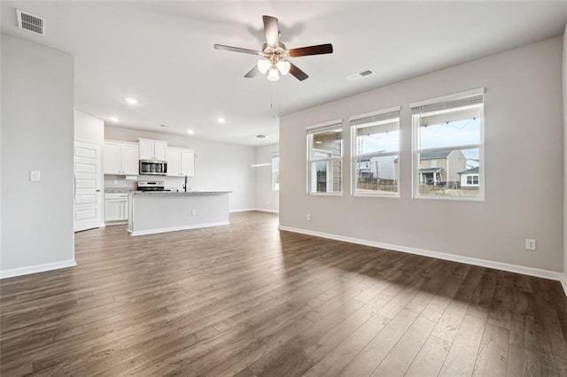 unfurnished living room with baseboards, visible vents, ceiling fan, and dark wood-type flooring