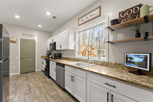 kitchen featuring light wood-style flooring, a sink, visible vents, white cabinetry, and black appliances