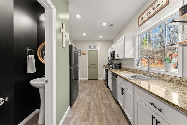 kitchen with light hardwood / wood-style flooring, black fridge, white cabinetry, and light stone counters