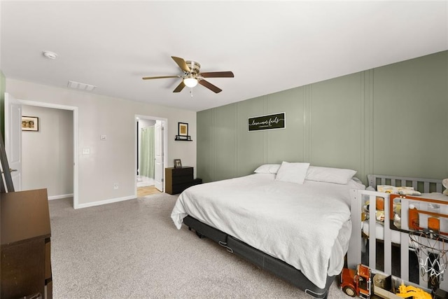 carpeted bedroom featuring visible vents, baseboards, ceiling fan, ensuite bathroom, and a decorative wall