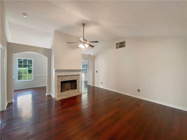 unfurnished living room with ceiling fan, a stone fireplace, dark hardwood / wood-style flooring, a textured ceiling, and lofted ceiling