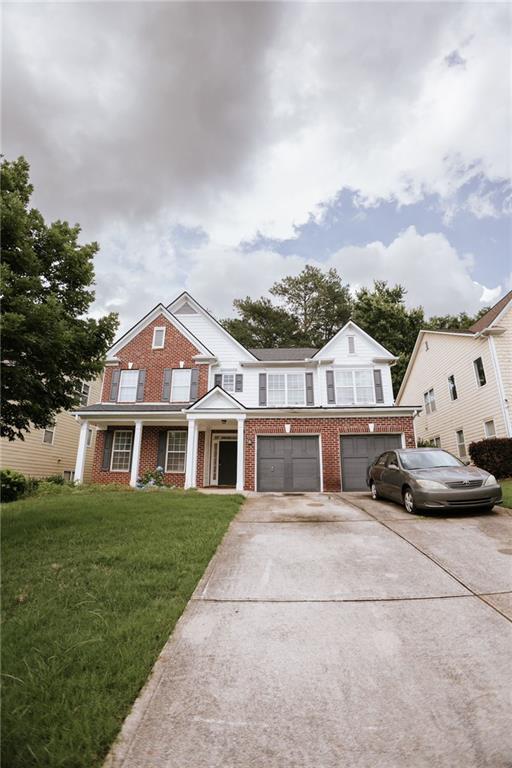 view of front of house featuring an attached garage, driveway, brick siding, and a front yard