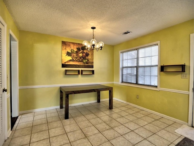 unfurnished dining area with tile patterned flooring, a textured ceiling, and a notable chandelier