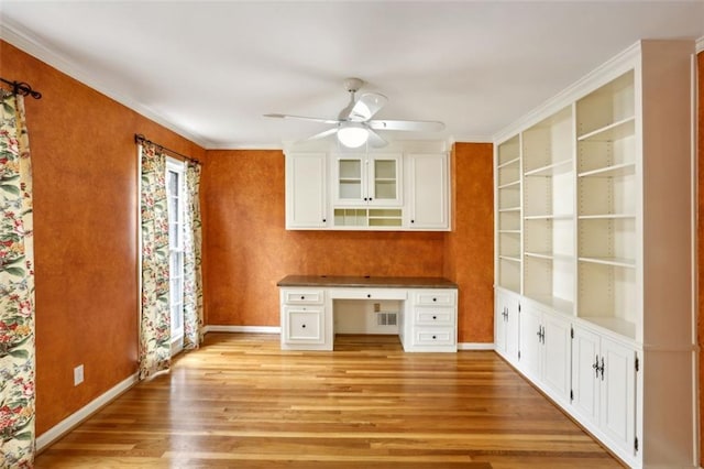 unfurnished office featuring built in shelves, ceiling fan, crown molding, built in desk, and light wood-type flooring