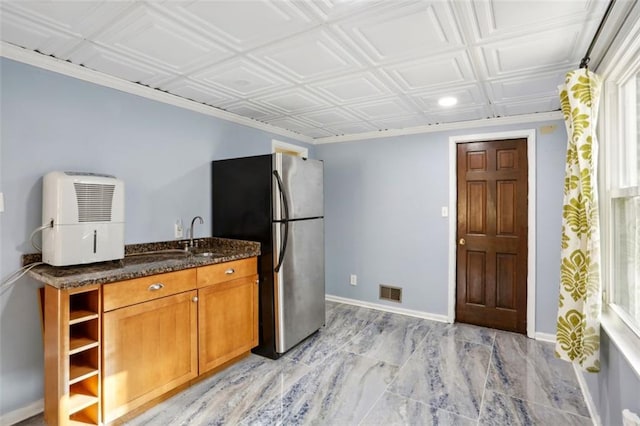 kitchen with dark stone countertops, crown molding, sink, and stainless steel refrigerator