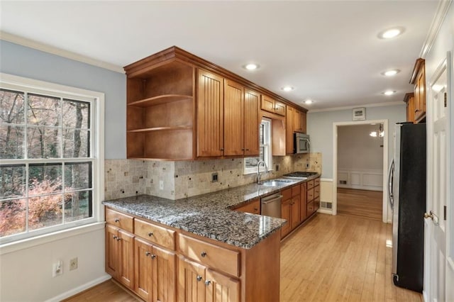 kitchen featuring dark stone counters, sink, appliances with stainless steel finishes, tasteful backsplash, and light hardwood / wood-style floors