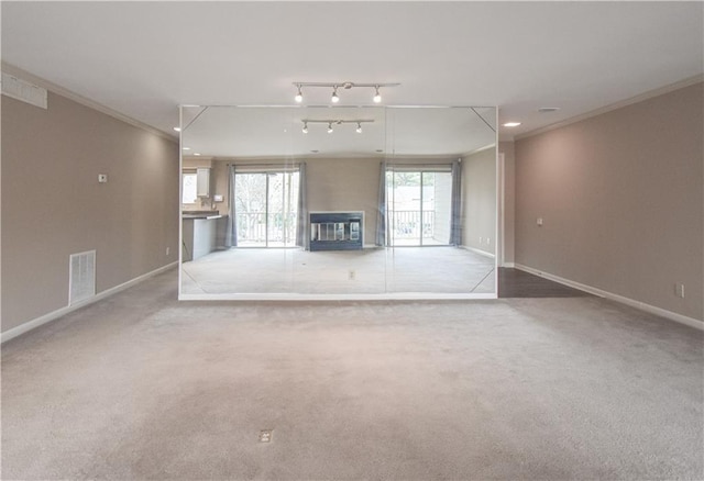 unfurnished living room with carpet, visible vents, ornamental molding, a glass covered fireplace, and baseboards