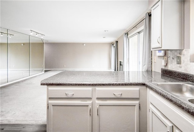 kitchen featuring a peninsula, a sink, white cabinetry, open floor plan, and tasteful backsplash