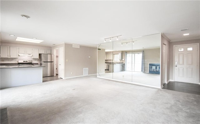 unfurnished living room featuring carpet floors, visible vents, ornamental molding, track lighting, and baseboards
