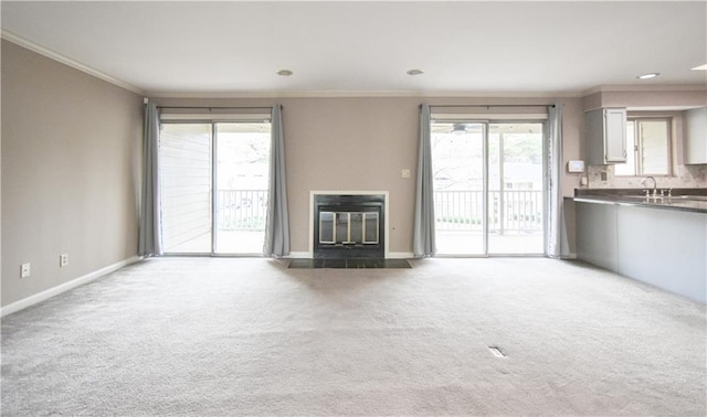 unfurnished living room with carpet floors, ornamental molding, a fireplace with flush hearth, and baseboards