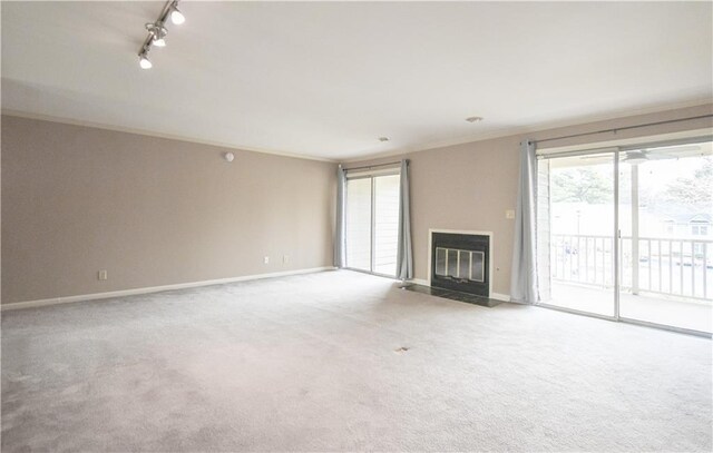 unfurnished living room with carpet, crown molding, rail lighting, a fireplace with flush hearth, and baseboards