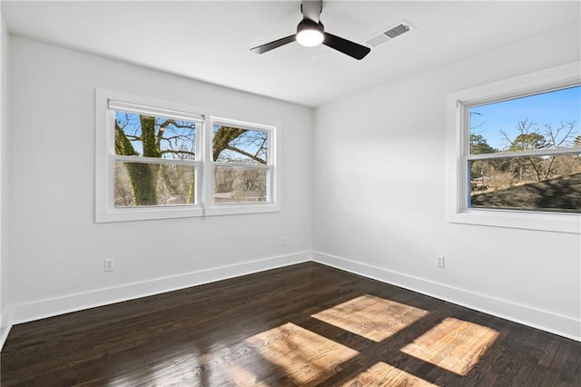 empty room featuring dark wood-style floors, a ceiling fan, visible vents, and baseboards