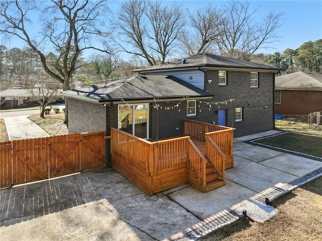 back of house with a shingled roof, a gate, brick siding, and fence