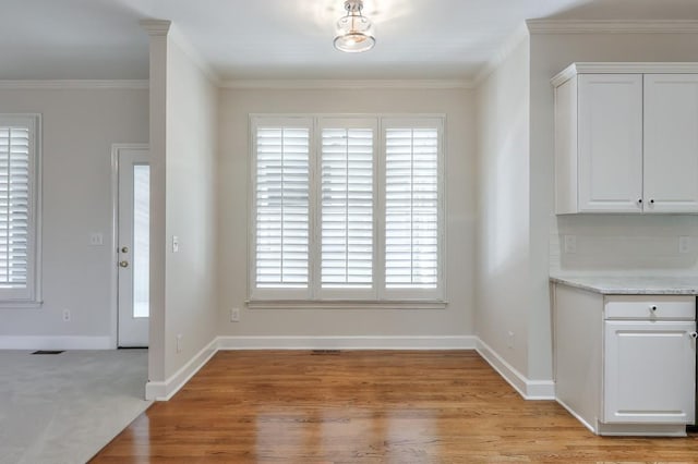 unfurnished dining area with light wood-type flooring, visible vents, ornamental molding, and baseboards