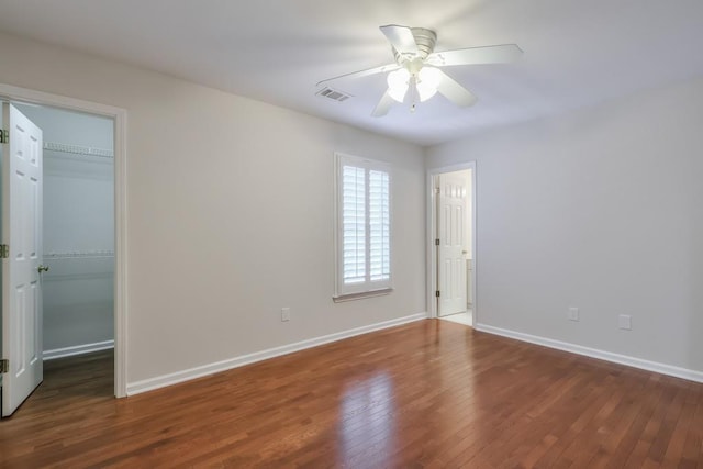 unfurnished bedroom with a spacious closet, wood-type flooring, visible vents, and baseboards