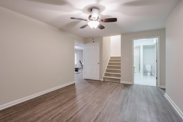 empty room featuring a ceiling fan, stairs, baseboards, and wood finished floors