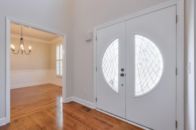 entryway featuring visible vents, baseboards, ornamental molding, light wood-type flooring, and an inviting chandelier