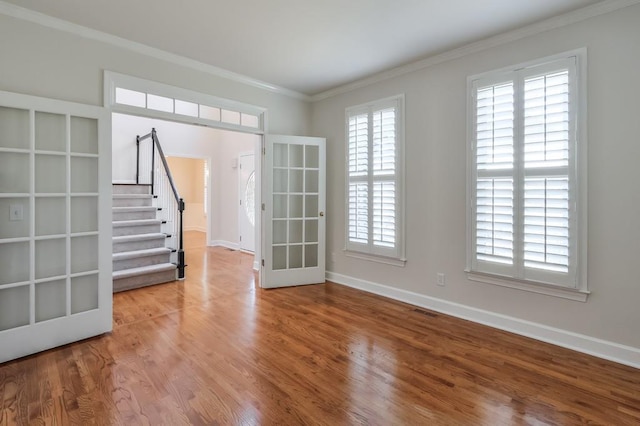 unfurnished room featuring wood finished floors, visible vents, baseboards, ornamental molding, and stairway