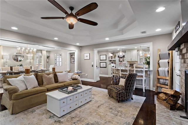 living room featuring a raised ceiling, ceiling fan, a brick fireplace, and hardwood / wood-style flooring