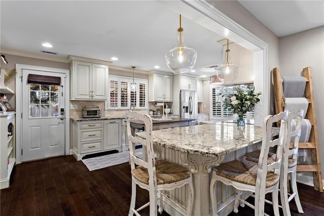 kitchen with a kitchen island, pendant lighting, stainless steel fridge with ice dispenser, white cabinets, and light stone counters