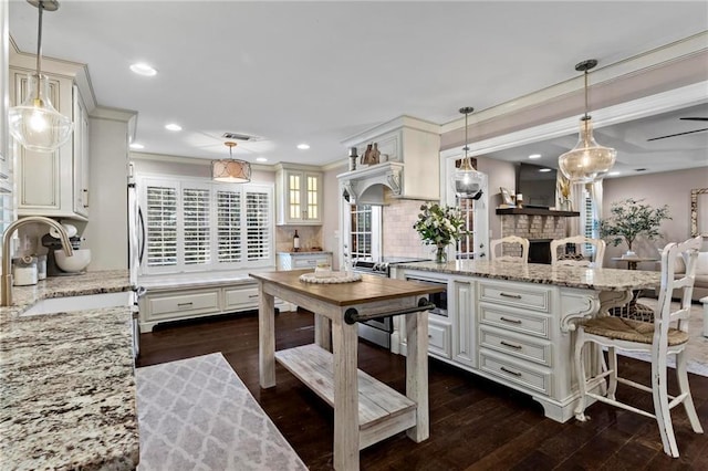 kitchen featuring light stone countertops, a kitchen island, decorative light fixtures, sink, and backsplash