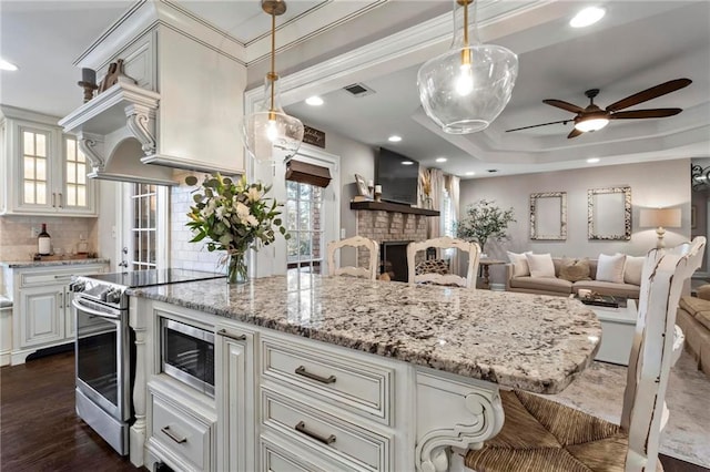 kitchen with ceiling fan, decorative backsplash, a raised ceiling, stainless steel electric stove, and a fireplace