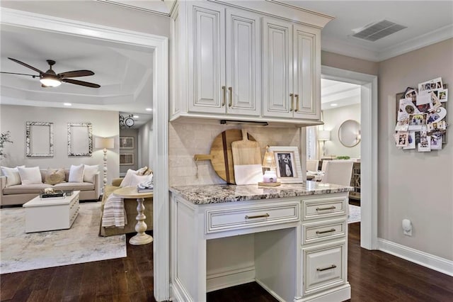 kitchen featuring ceiling fan, decorative backsplash, dark wood-type flooring, crown molding, and light stone counters