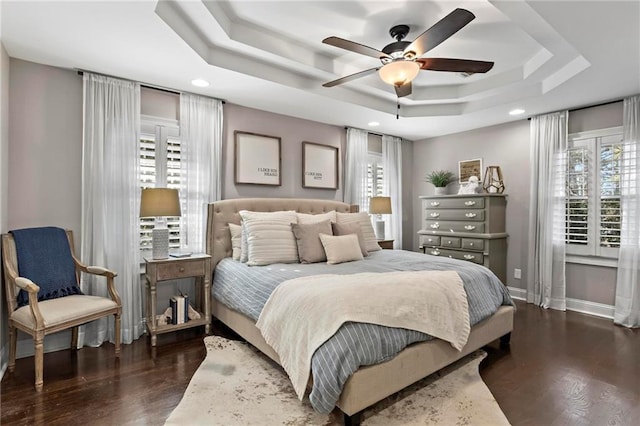 bedroom with ceiling fan, dark hardwood / wood-style floors, a tray ceiling, and multiple windows