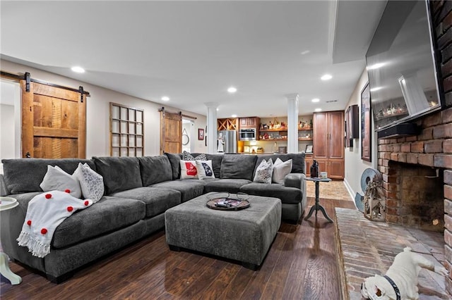 living room featuring a brick fireplace, dark hardwood / wood-style flooring, and a barn door