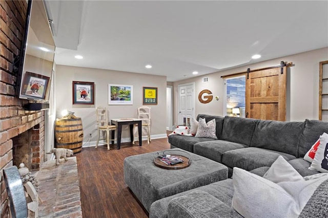 living room featuring a barn door, dark wood-type flooring, and a brick fireplace